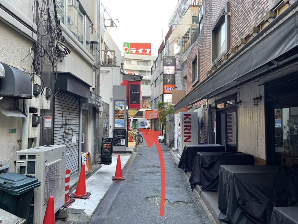 ラーメン屋さんの脇道の写真。突き当たりにスーパーマーケットが見えます。突き当たりまで直進して左に曲がる指示の矢印画像が貼り付けてあります。