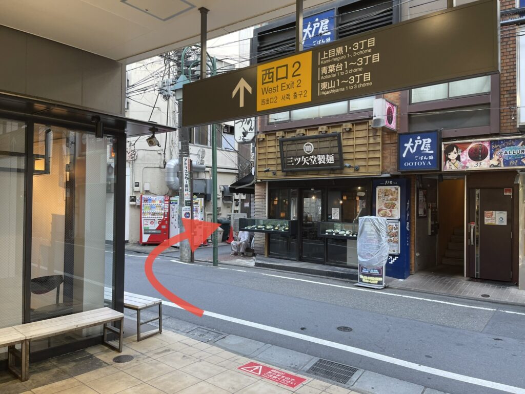 中目黒駅の西口2番出口を出るところの写真。目の前にあるラーメン屋さんの脇道へ進む指示の矢印画像が貼り付けてあります。